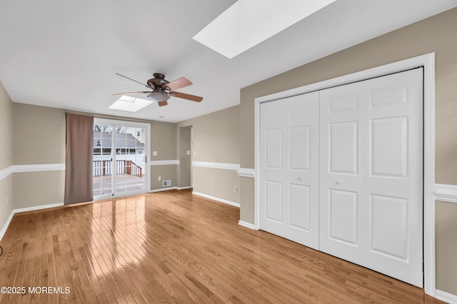 unfurnished bedroom featuring a skylight, light wood-type flooring, a closet, ceiling fan, and access to exterior