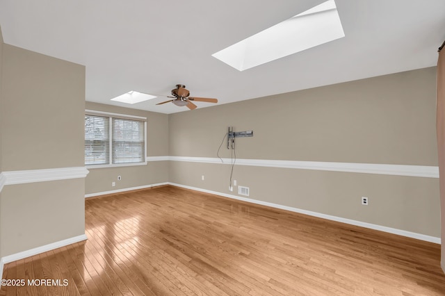 spare room with light hardwood / wood-style flooring, a skylight, and ceiling fan