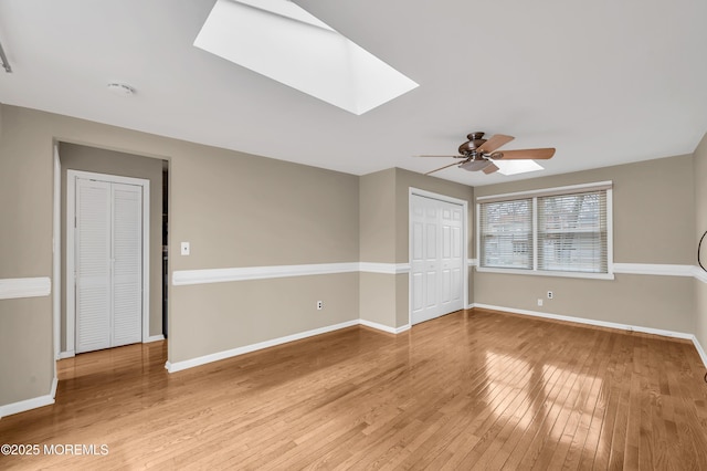 empty room with ceiling fan, a skylight, and hardwood / wood-style floors