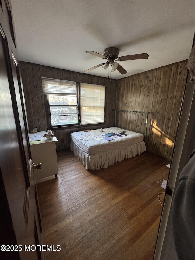 bedroom with ceiling fan, dark hardwood / wood-style floors, and wooden walls