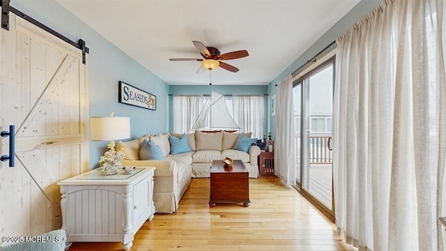 living room with light wood-style floors, a barn door, and ceiling fan