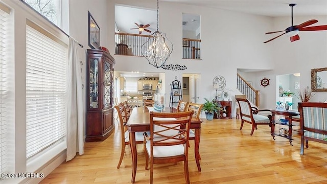 dining room with a towering ceiling, stairway, light wood finished floors, and ceiling fan with notable chandelier