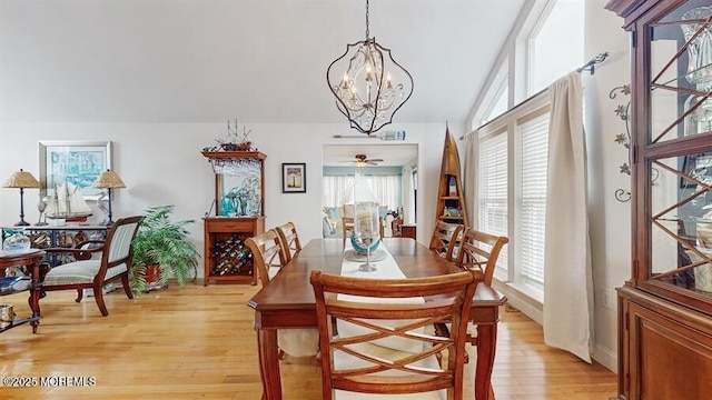 dining space with an inviting chandelier, light wood-style flooring, and vaulted ceiling