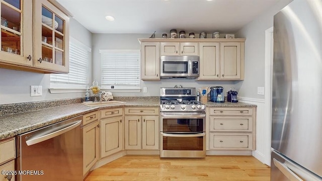 kitchen with light wood finished floors, appliances with stainless steel finishes, cream cabinetry, and a sink