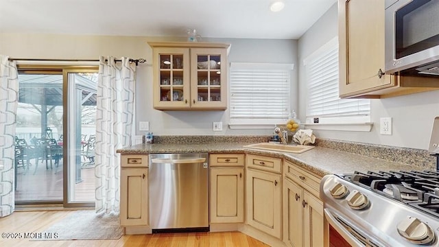 kitchen featuring glass insert cabinets, appliances with stainless steel finishes, cream cabinets, light wood-type flooring, and a sink