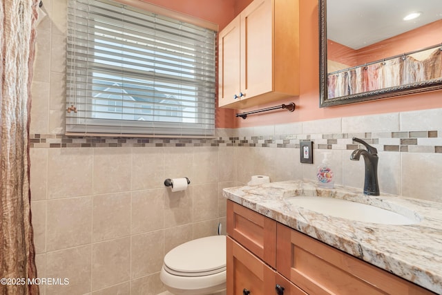 bathroom featuring vanity, tile walls, and toilet