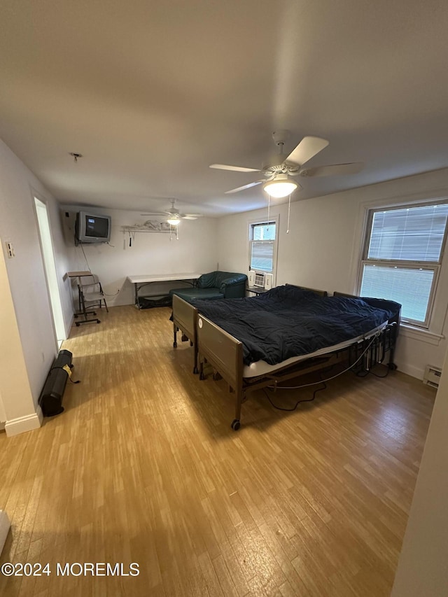 bedroom featuring baseboard heating, cooling unit, ceiling fan, and light hardwood / wood-style flooring