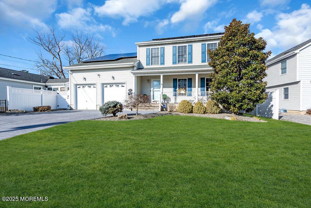 view of front of property featuring a garage, covered porch, a front yard, and solar panels