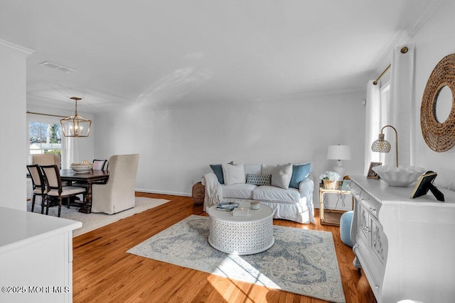 living room featuring ornamental molding, a chandelier, and light hardwood / wood-style floors