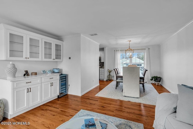 dining space featuring a notable chandelier, ornamental molding, beverage cooler, and light wood-type flooring