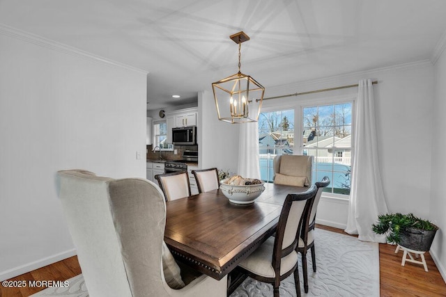 dining space featuring an inviting chandelier, sink, ornamental molding, and light wood-type flooring