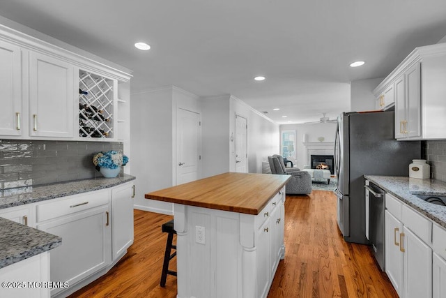 kitchen with butcher block countertops, hardwood / wood-style flooring, a kitchen breakfast bar, a center island, and white cabinets