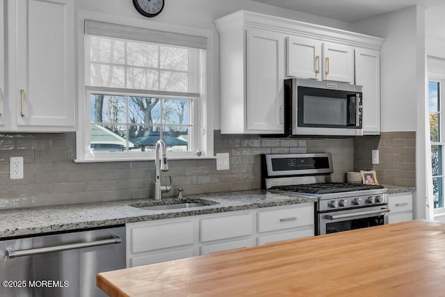 kitchen featuring sink, tasteful backsplash, appliances with stainless steel finishes, light stone countertops, and white cabinets