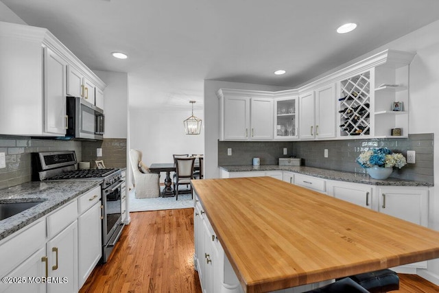 kitchen with pendant lighting, butcher block countertops, white cabinets, stainless steel appliances, and light wood-type flooring