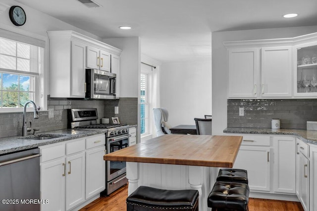 kitchen with appliances with stainless steel finishes, butcher block counters, sink, and white cabinets