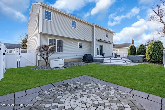 back of house with a hot tub, a patio, and a lawn