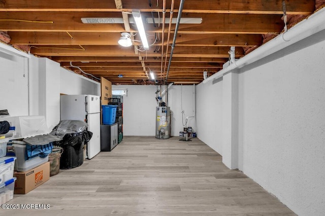 basement with light hardwood / wood-style flooring, water heater, and white refrigerator