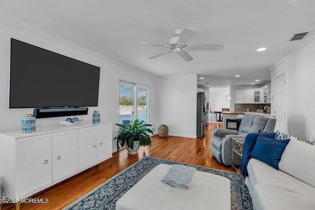 living room featuring wood-type flooring, ornamental molding, and ceiling fan