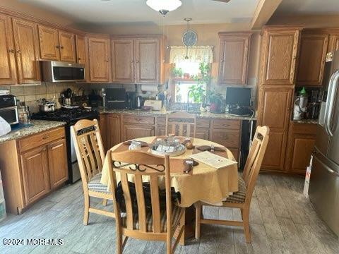 kitchen with pendant lighting, appliances with stainless steel finishes, backsplash, light stone counters, and light hardwood / wood-style floors