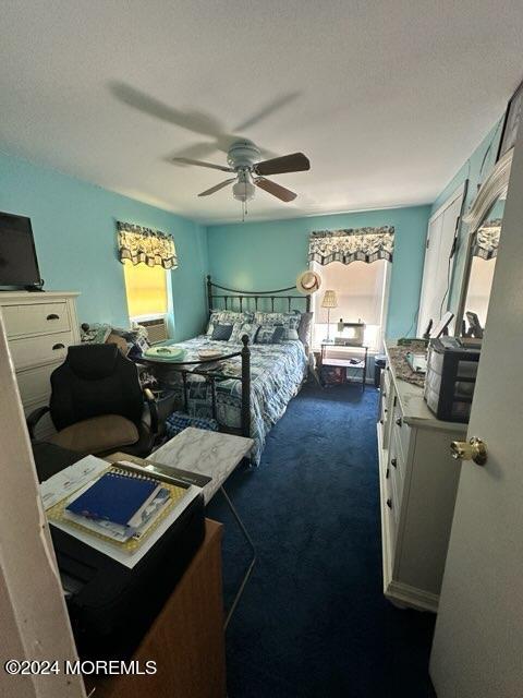 bedroom featuring ceiling fan, a textured ceiling, multiple windows, and dark colored carpet