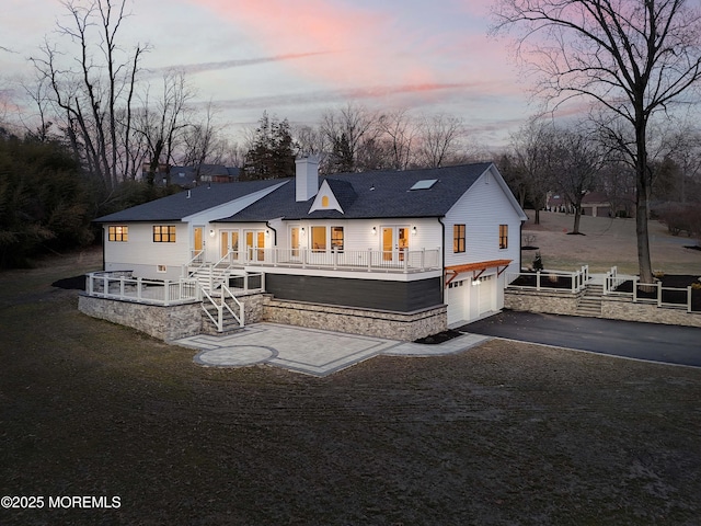 rear view of house featuring driveway, a shingled roof, a chimney, an attached garage, and stairs