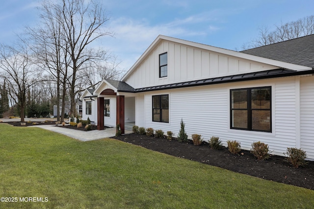 view of front facade featuring roof with shingles, board and batten siding, a standing seam roof, a patio area, and a front lawn