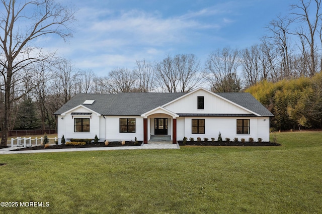 view of front facade with a shingled roof, metal roof, fence, and a front lawn