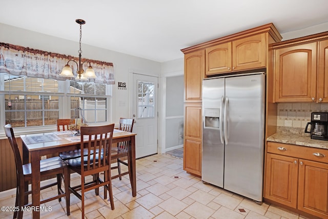 kitchen with stainless steel fridge, a chandelier, decorative backsplash, hanging light fixtures, and light stone counters