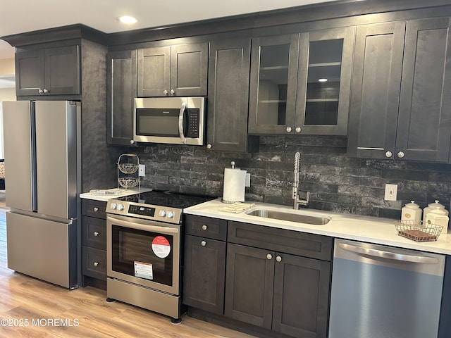 kitchen with stainless steel appliances, sink, decorative backsplash, and light wood-type flooring