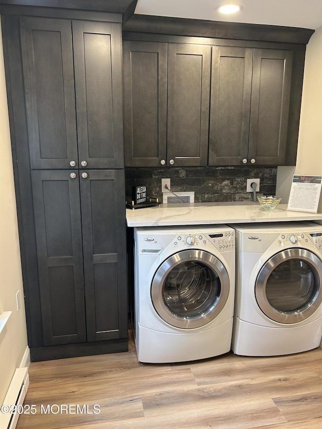 washroom with a baseboard heating unit, washer and clothes dryer, light hardwood / wood-style floors, and cabinets