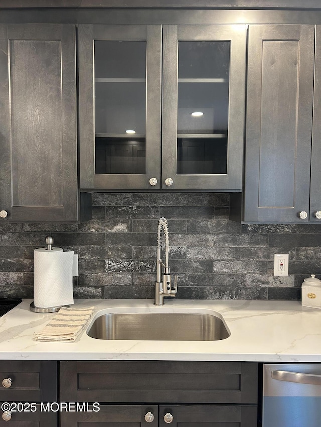 kitchen featuring light stone counters, sink, backsplash, and stainless steel dishwasher