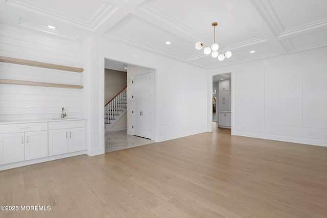 interior space featuring light wood finished floors, a decorative wall, a sink, coffered ceiling, and stairs