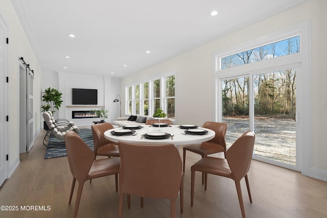 dining room featuring a barn door, a glass covered fireplace, light wood-style flooring, and recessed lighting