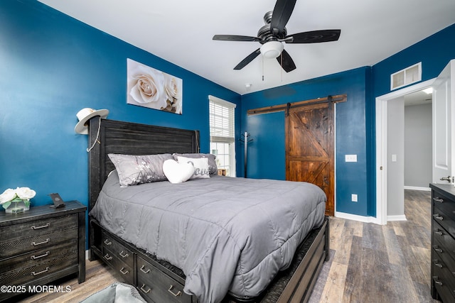 bedroom featuring wood-type flooring, a barn door, and ceiling fan