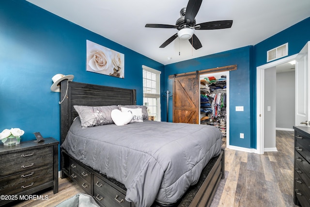 bedroom with wood-type flooring, a walk in closet, ceiling fan, a barn door, and a closet