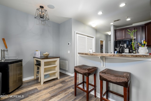 kitchen with pendant lighting, dark hardwood / wood-style flooring, a kitchen bar, black fridge, and dark brown cabinets