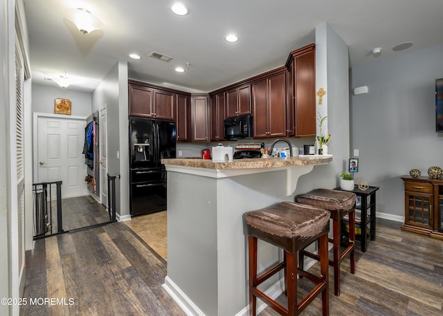 kitchen with dark hardwood / wood-style floors, black appliances, sink, a kitchen breakfast bar, and kitchen peninsula