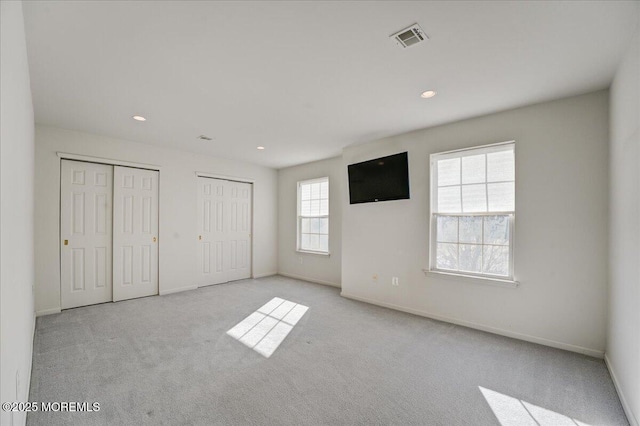 unfurnished bedroom with two closets and light colored carpet