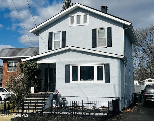 traditional style home with a fenced front yard, a chimney, and stucco siding