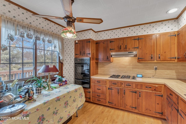 kitchen with stainless steel gas stovetop, black double oven, ceiling fan, crown molding, and light wood-type flooring