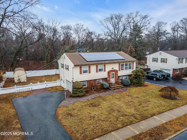 bi-level home featuring a garage, a front lawn, and solar panels