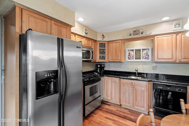 kitchen with sink, appliances with stainless steel finishes, dark stone countertops, and light hardwood / wood-style floors