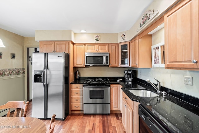 kitchen featuring light brown cabinetry, light wood-type flooring, stainless steel appliances, dark stone counters, and sink