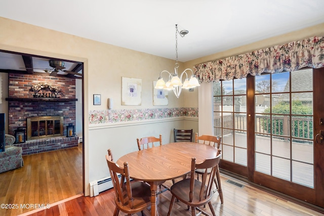 dining space featuring a fireplace, a baseboard radiator, wood-type flooring, and ceiling fan with notable chandelier