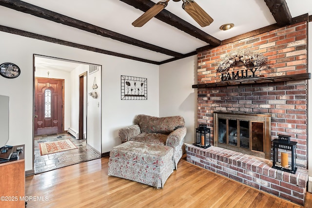 living room with beam ceiling, ceiling fan, wood-type flooring, and a fireplace