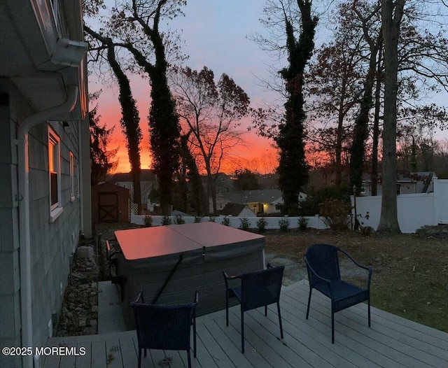 deck at dusk with a storage shed and a covered hot tub