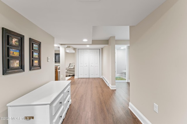 corridor with a baseboard radiator, decorative columns, and wood-type flooring