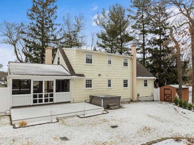 snow covered property with a storage shed, a hot tub, and a sunroom