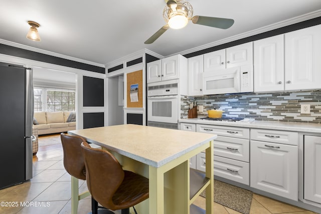 kitchen featuring a breakfast bar, white cabinets, light tile patterned floors, crown molding, and white appliances