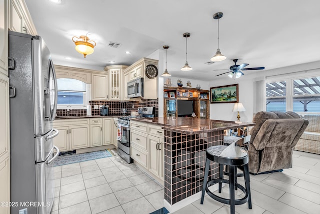 kitchen with pendant lighting, a breakfast bar area, stainless steel appliances, and cream cabinetry